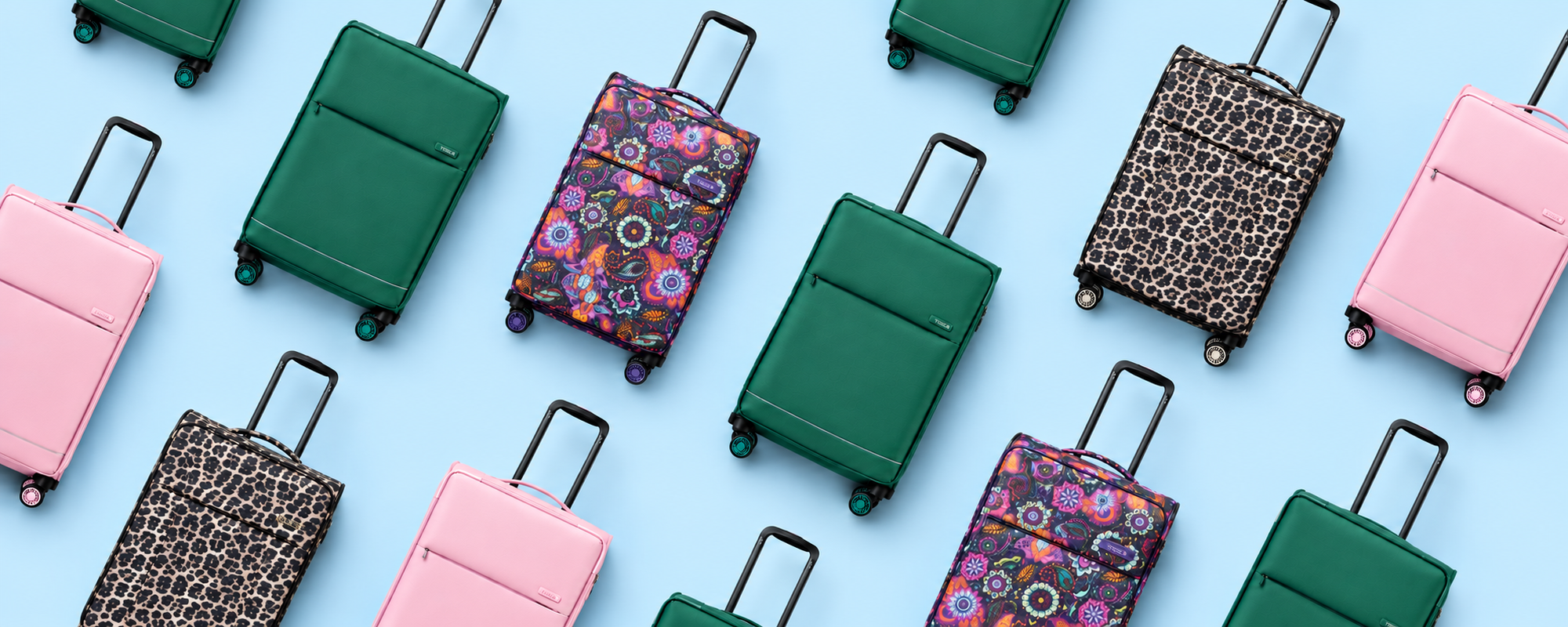 A flat-lay arrangement of multiple rolling So Lite suitcases in pink, green, leopard print, and floral patterns on a light blue background.